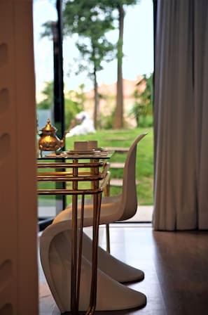 A modern dining area with a glass table, white chairs, and a brass tea set.