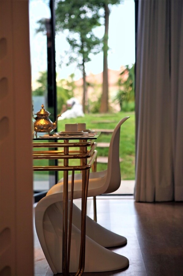 A modern dining area with a glass table, white chairs, and a brass tea set.