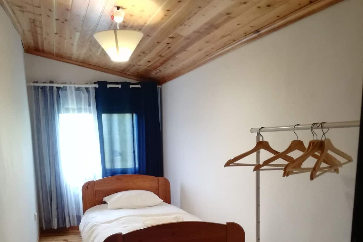 Una habitación pequeña con una cama de madera, un perchero y una ventana con cortinas.