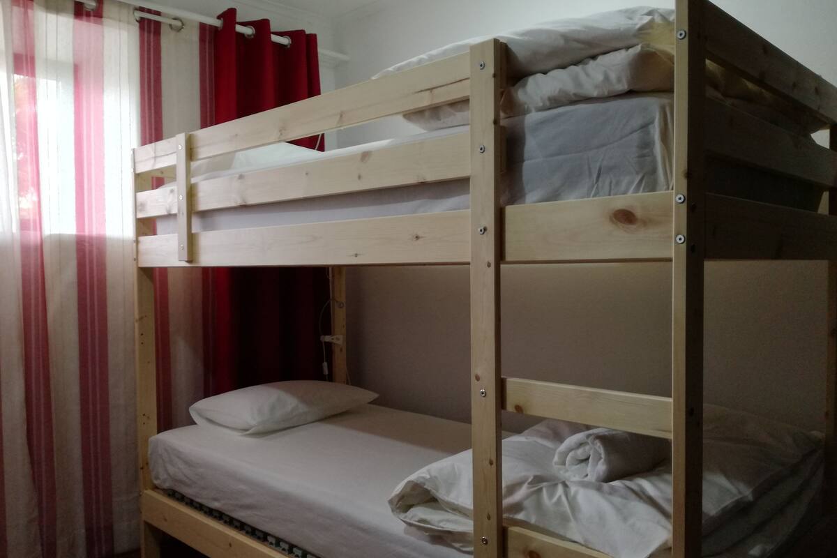 Una cama litera con ropa de cama blanca y una cortina roja al fondo.
