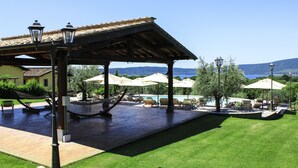 Un espacio exterior techado con piscina, sillones de descanso y sombrillas.