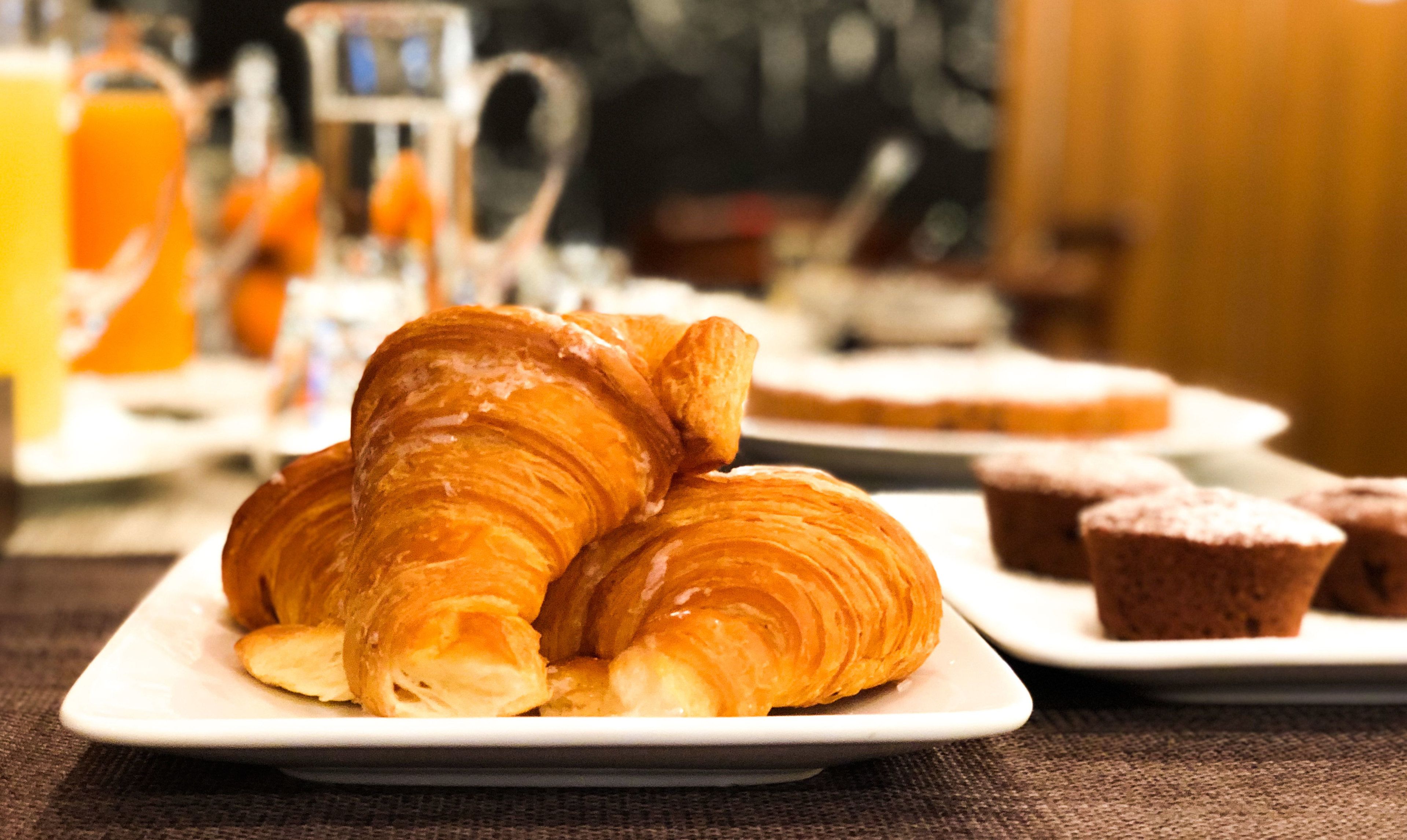 A breakfast setting with croissants and muffins on plates, a coffee machine, and a glass of orange juice.