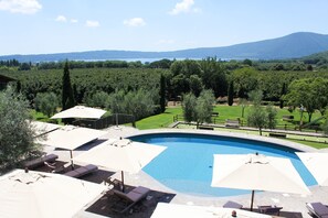 A swimming pool with lounge chairs and umbrellas, surrounded by a landscaped garden and a view of a lake and mountains.