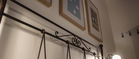 Una cama con cabecera de metal, una lámpara fijada a la pared y cuadros enmarcados.