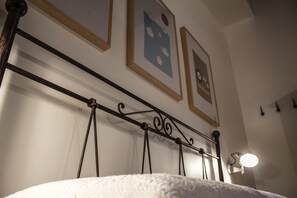 Una cama con cabecera de metal, una lámpara fijada a la pared y cuadros enmarcados.