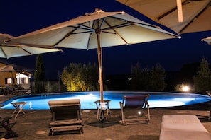 Una piscina con sillas de descanso y sombrillas, rodeada por una valla y árboles.