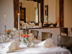 Une table dressée pour le dîner, avec des nappes blanches, des bougies et des arrangements floraux.