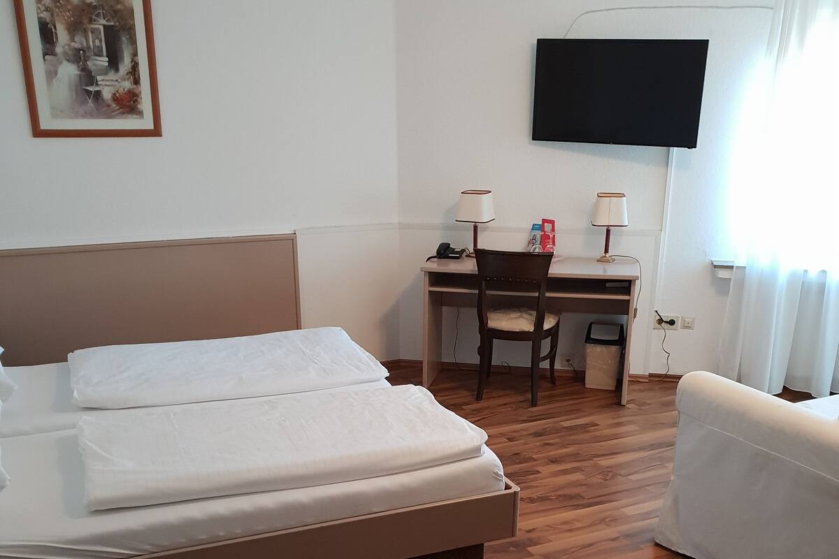 Une chambre d’hôtel avec un lit, un bureau, une chaise, une télévision et une fenêtre avec des rideaux.