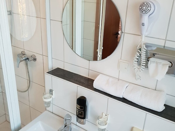Une salle de bain équipée d’une douche, d’un sèche-cheveux, d’un porte-serviettes et d’un miroir.