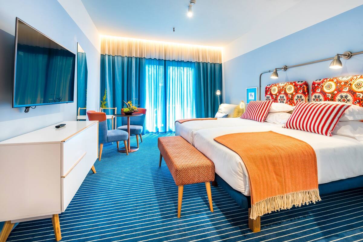 Une chambre d’hôtel avec un lit, un bureau, une télévision, une chaise et une fenêtre avec des rideaux.