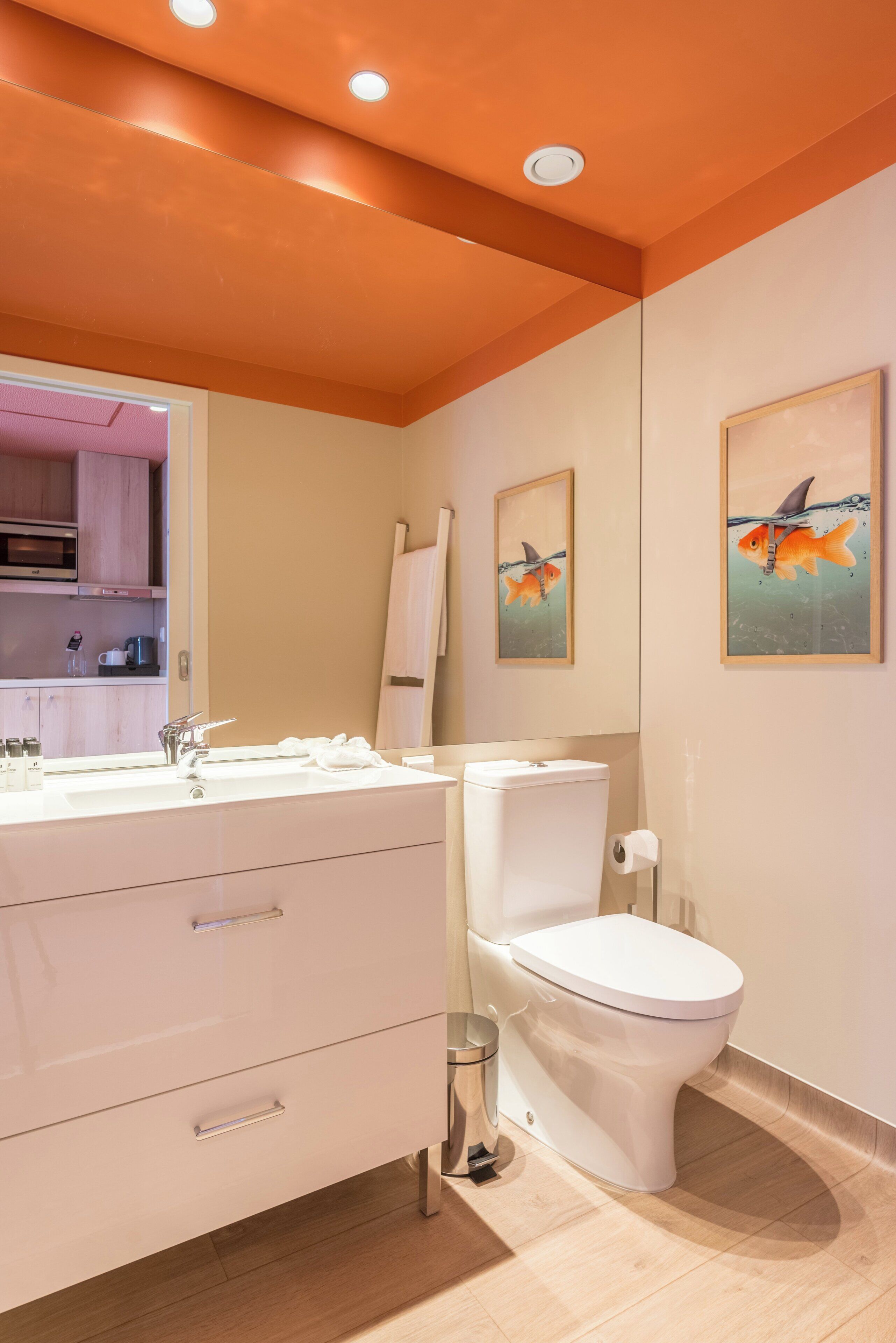 Une salle de bain moderne avec un lavabo, des toilettes et un meuble-lavabo blancs. Des tableaux encadrés ornent le mur et un luminaire est fixé au plafond.