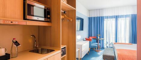 Een hotelkamer met een kitchenette, een bed, een bureau en een stoel.