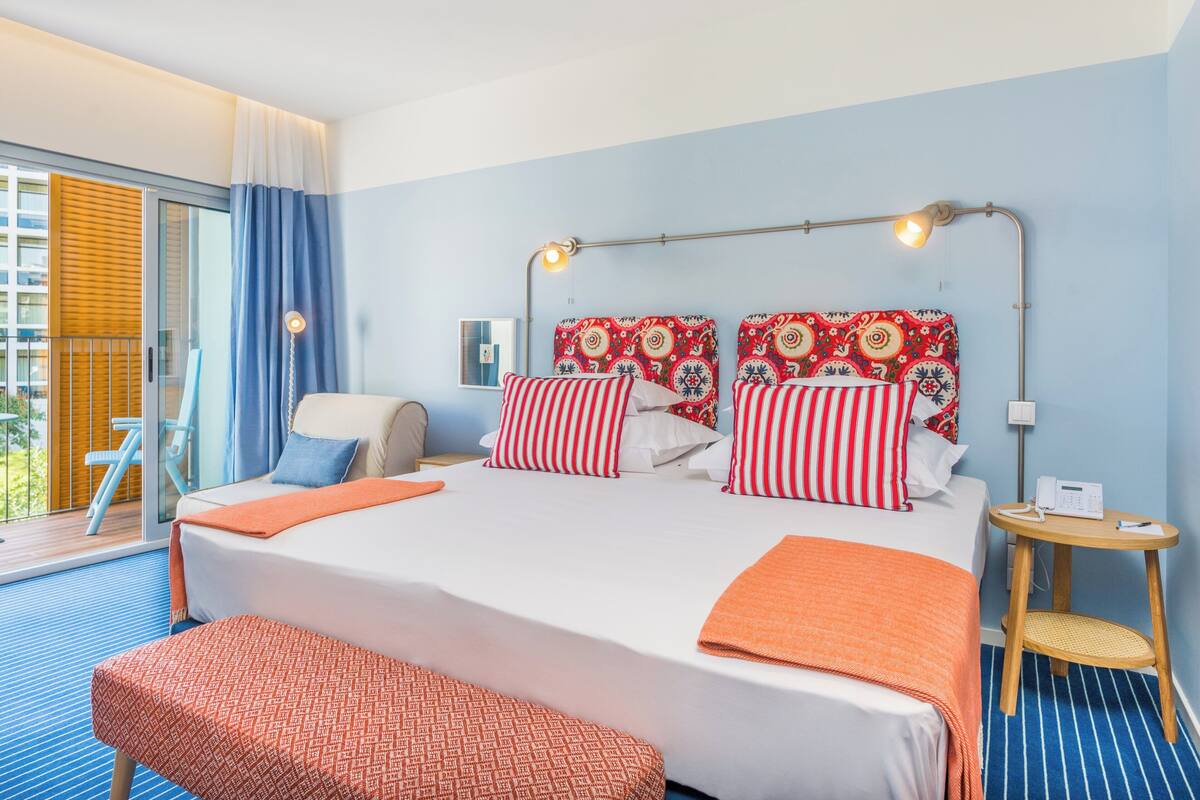 Une chambre d’hôtel avec un grand lit, une table de chevet avec une lampe, une chaise et une vue sur l’extérieur.