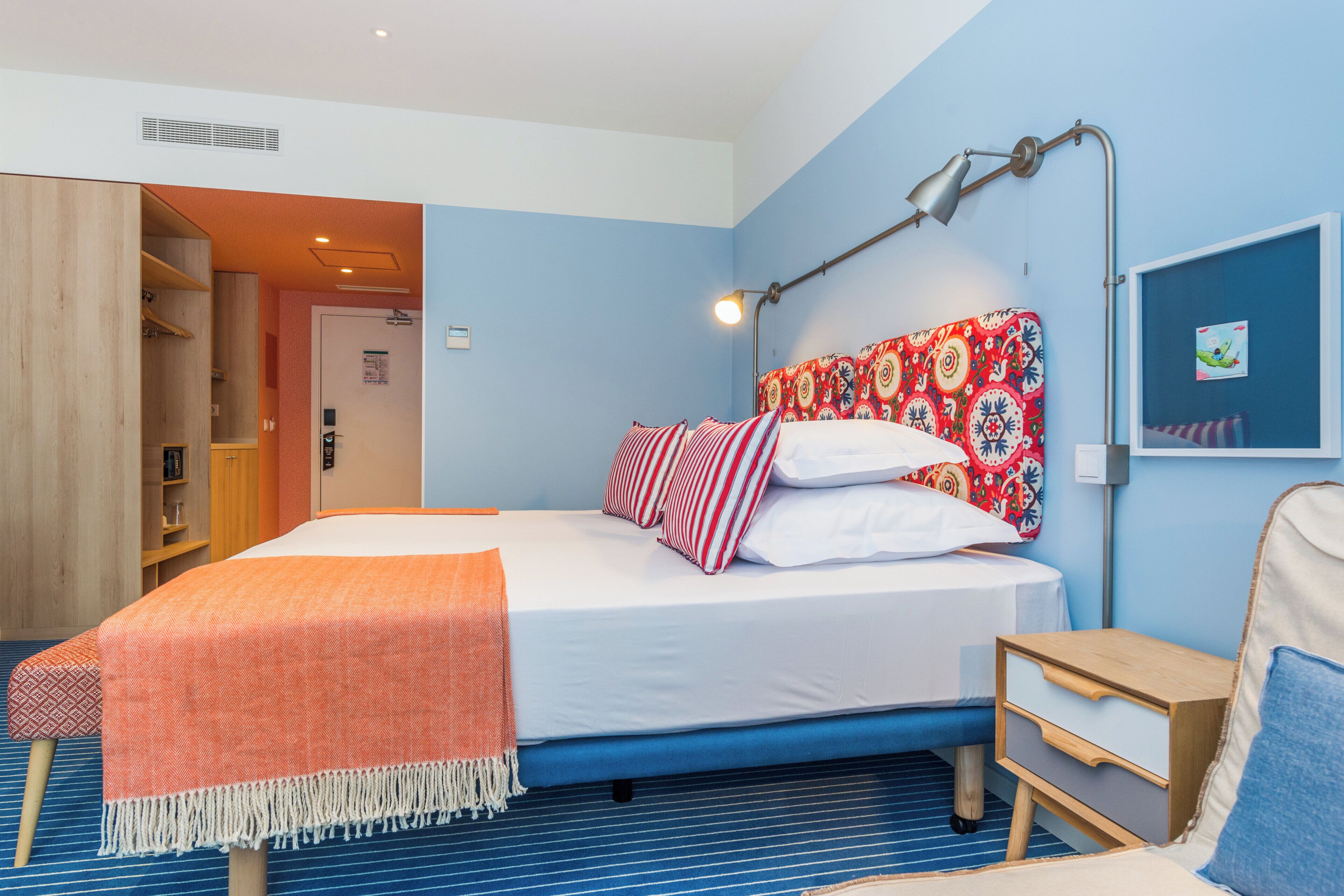 A hotel room with a bed, a bedside table, a lamp, a wardrobe, and a door.