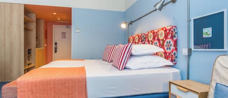 A hotel room with a bed, a bedside table, a lamp, a wardrobe, and a door.