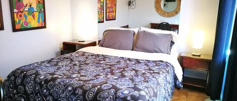 A hotel room with a large bed, a TV, a mirror, and artwork on the walls.