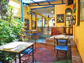 A restaurant with yellow walls, blue chairs, and a variety of plants. Tables are set with plates and cutlery. - Hotel Casa 69 (San José)