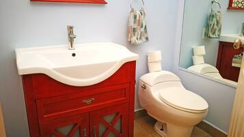 A bathroom with a white sink, red vanity, and a white toilet.