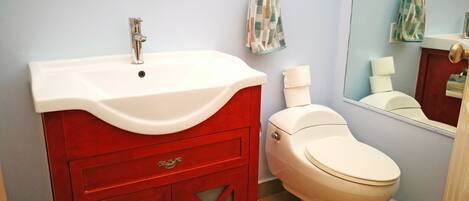 Un baño con un lavamanos blanco, tocador rojo y un inodoro blanco.