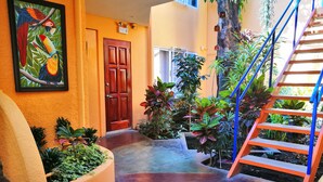 A hallway with a wooden door, a staircase, and various plants. - Hotel Casa 69 (San José)
