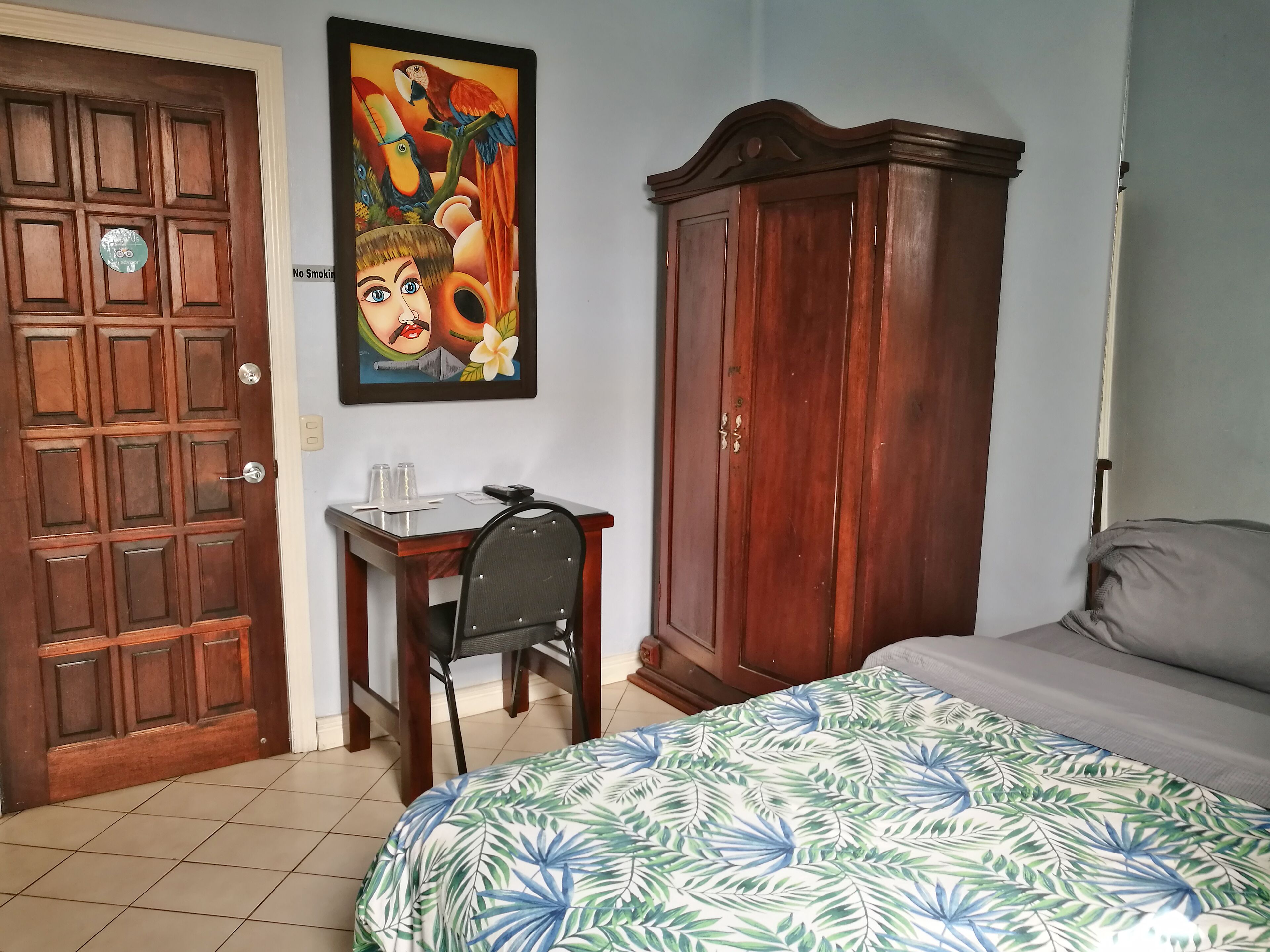 Un dormitorio con cama, un armario de madera, un escritorio con silla y un cuadro en la pared.