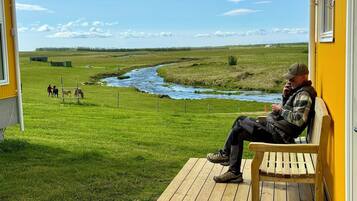 Una terraza de madera con un banco que da a un río y un campo cubierto de hierba.
