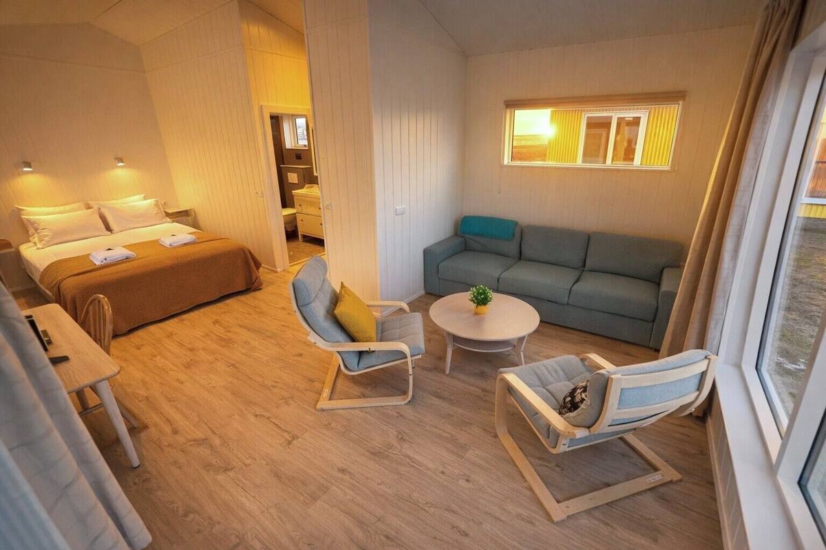 A hotel room with a bed, a sofa, two armchairs, a small table, and a window with curtains.