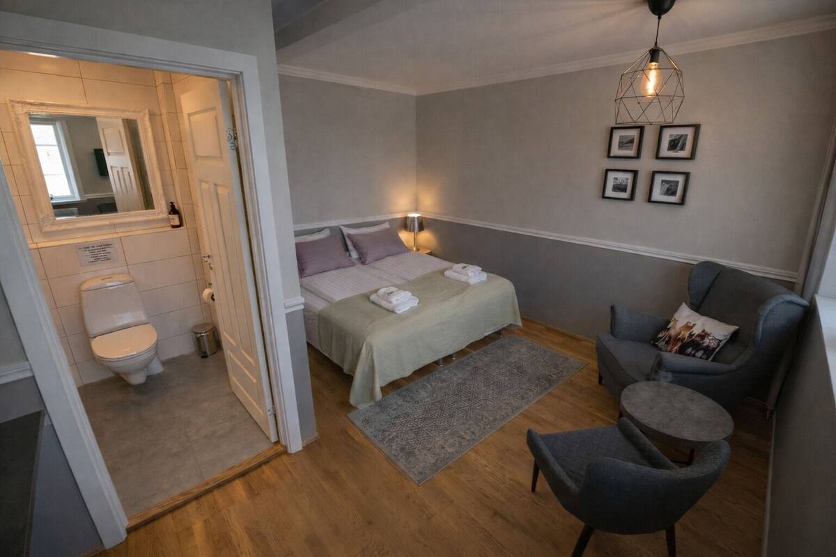 A bedroom with a bed, bedside tables, a chair, a rug, and a hanging light fixture.