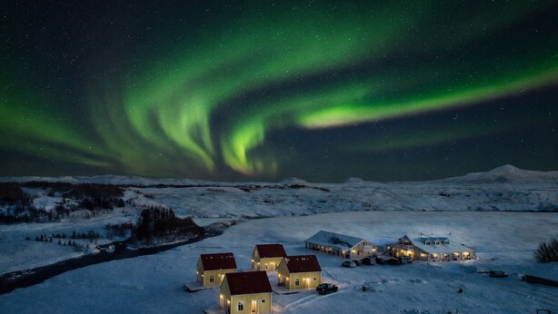 A snow-covered landscape with houses under a starry night sky and the Northern Lights. - Hotel Lækur (Rangárþing ytra)