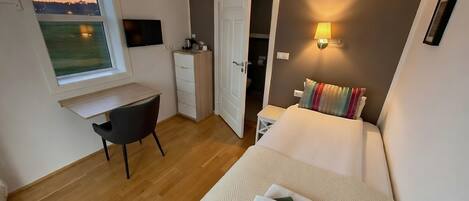 Une chambre à coucher comprenant un lit, un bureau, une chaise, une armoire et une fenêtre donnant sur l’extérieur.