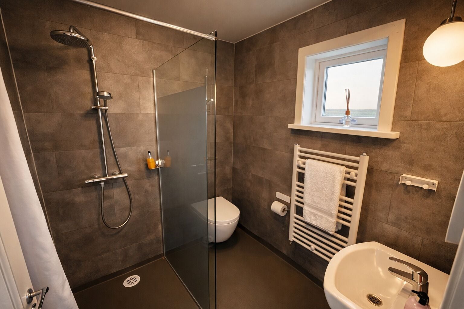 A modern bathroom with a glass-enclosed shower, a toilet, a sink, and a window above the sink.