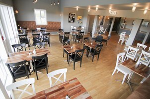 A restaurant with multiple tables and chairs, wooden flooring, and a mix of black and white chairs.