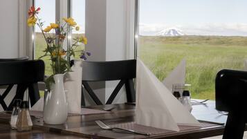 Una mesa de comedor con un florero, saleros y pimenteros, y vista a una montaña.