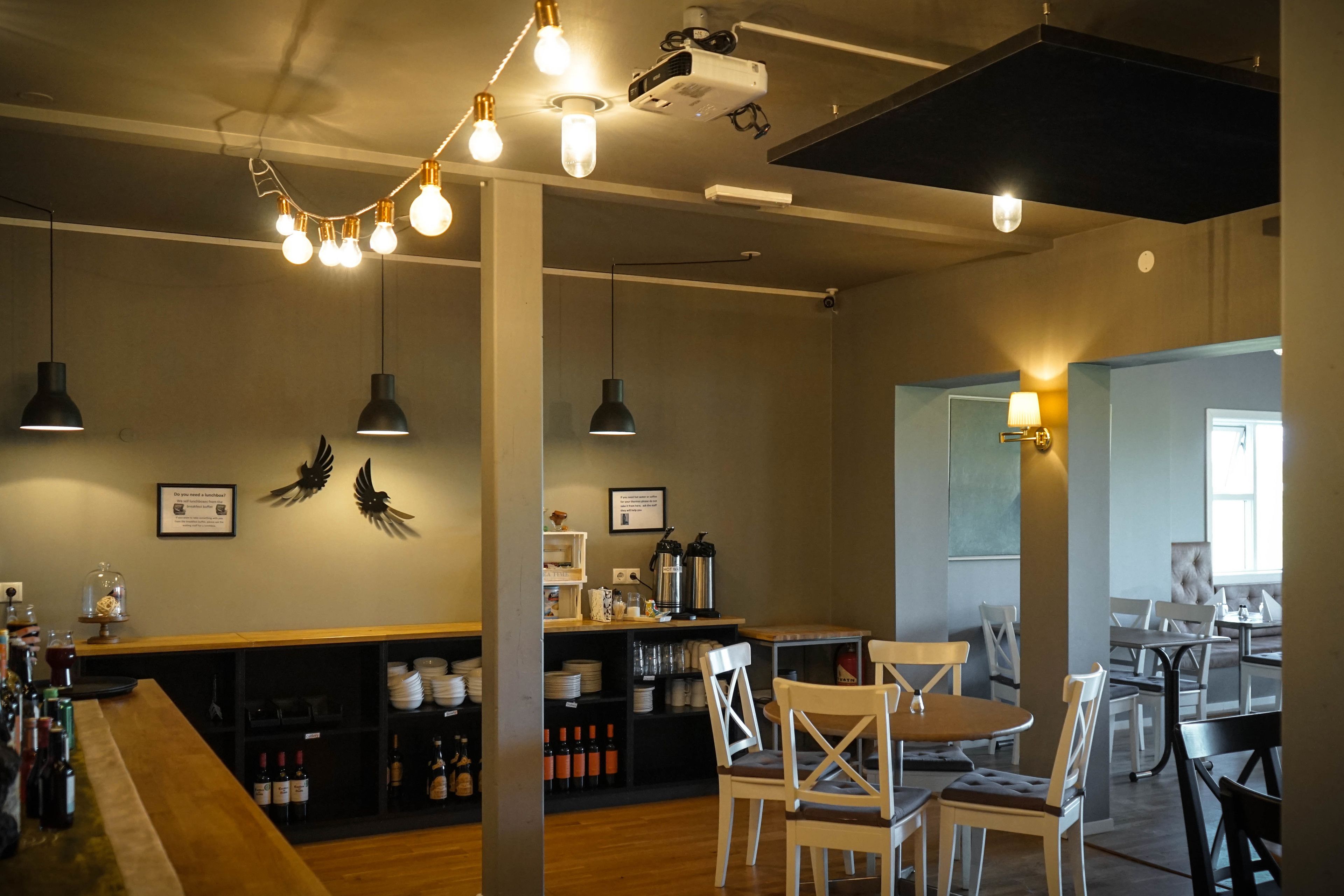 A modern restaurant interior with a bar area, wooden tables, and hanging light fixtures.