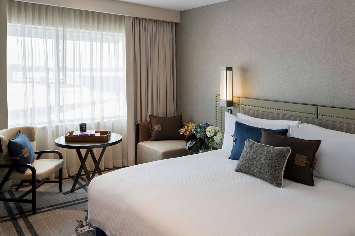 A hotel room with a large bed, a small table with a tray, a chair, and a sofa.