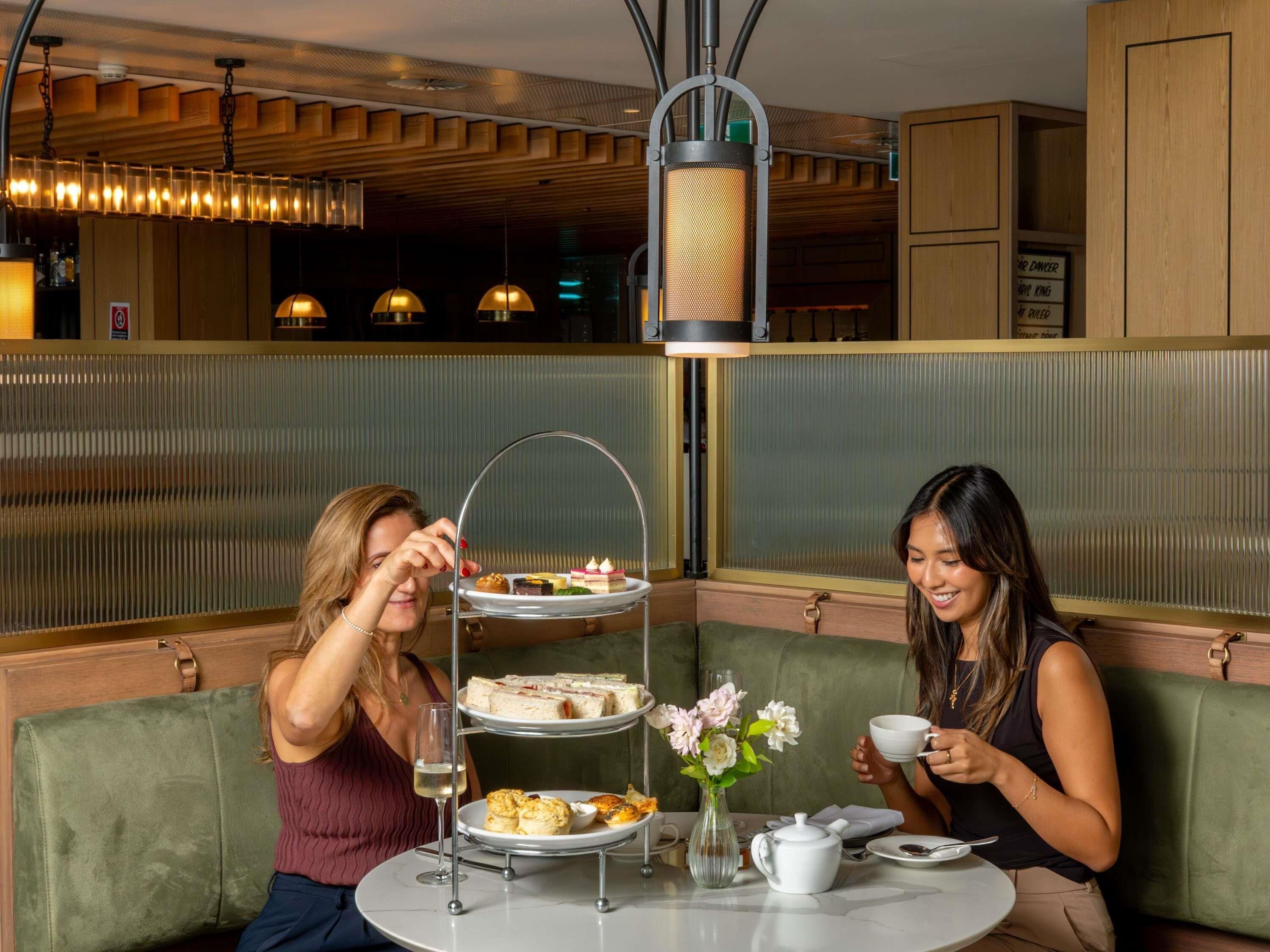 Un coin repas agrémenté d’un présentoir à étages pour les desserts, d’un vase rempli de fleurs et d’une table sur laquelle sont posés une théière et des tasses.
