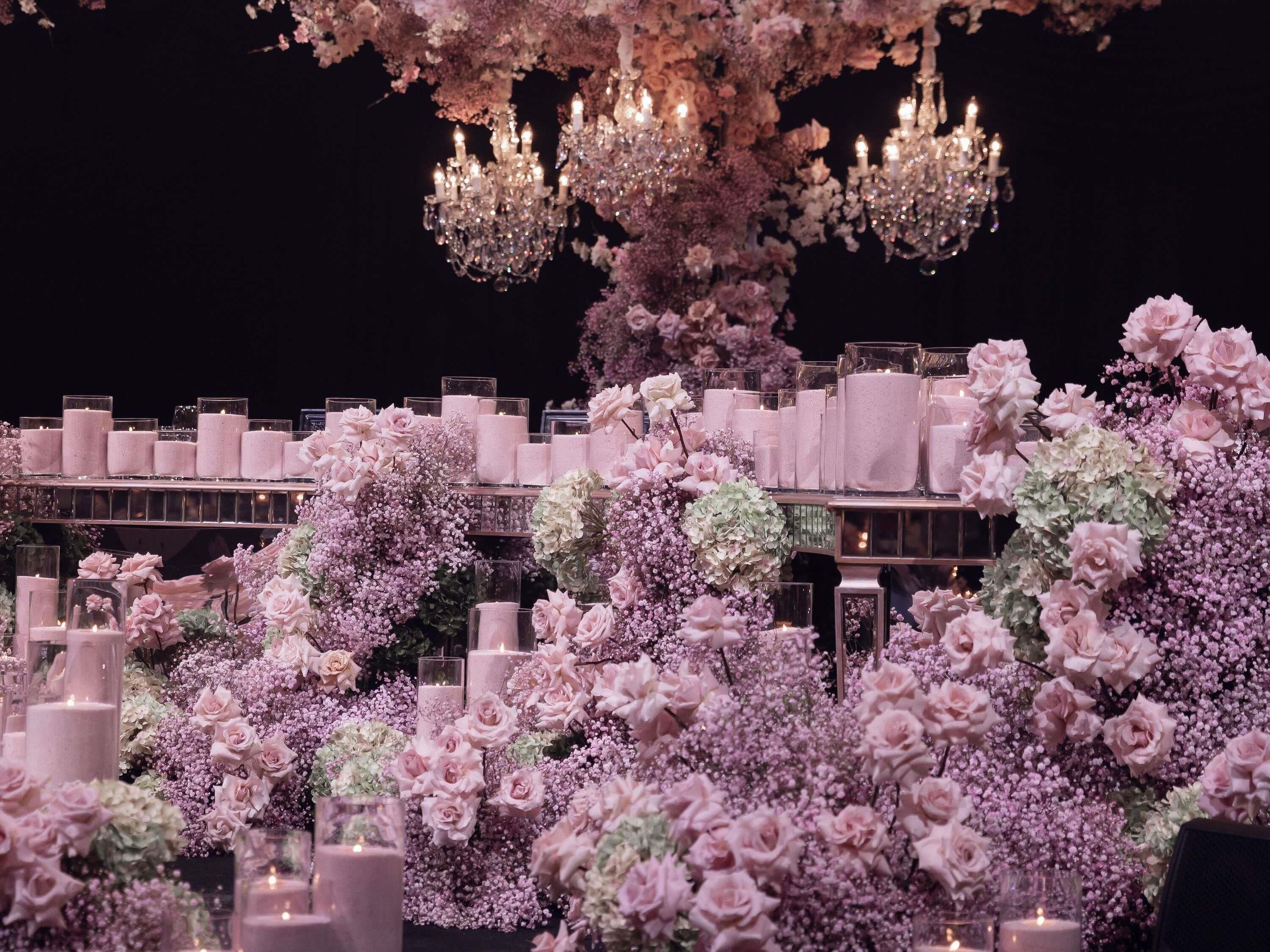 Um espaço para eventos luxuoso, com lustres, arranjos florais e velas.