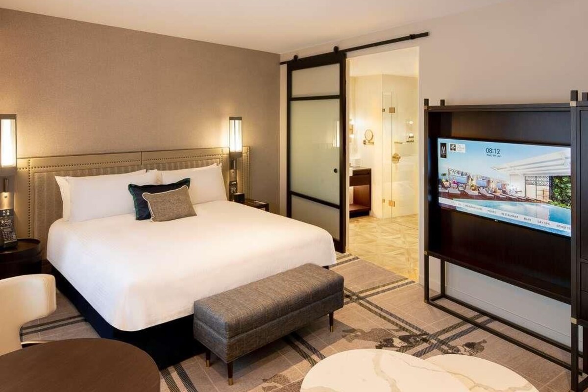 A hotel room with a bed, bedside table, TV, and a sliding door leading to a bathroom.