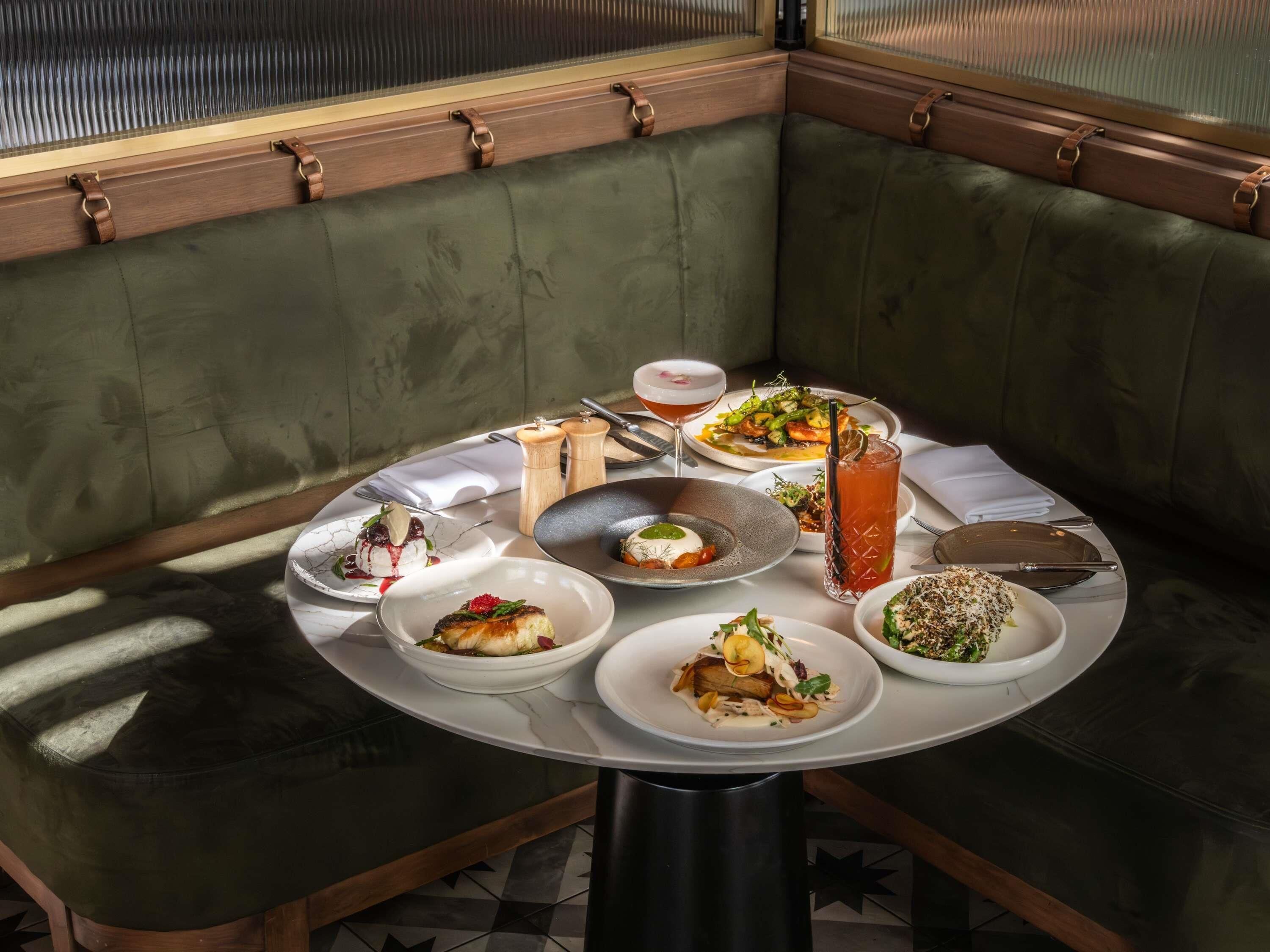 A dining table with various dishes, a drink, and a knife in a corner seating area with a cushioned bench.