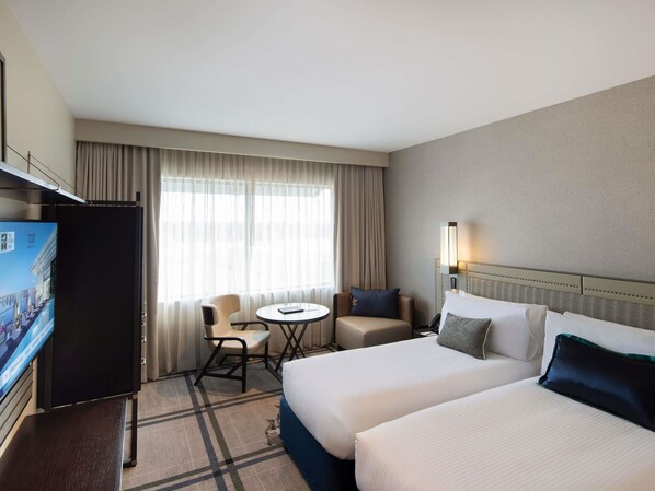 Habitación de hotel con dos camas, un escritorio, una silla, un televisor y una ventana con cortinas.