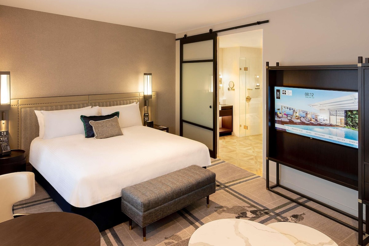 A hotel room with a bed, bedside tables, a TV, and a sliding door leading to a bathroom.
