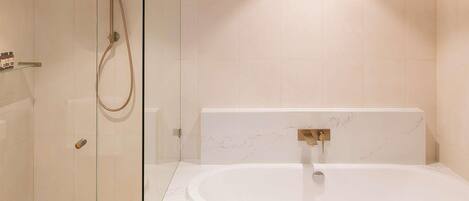 A modern bathroom with a glass-enclosed shower, a freestanding bathtub, and a marble-tiled wall.