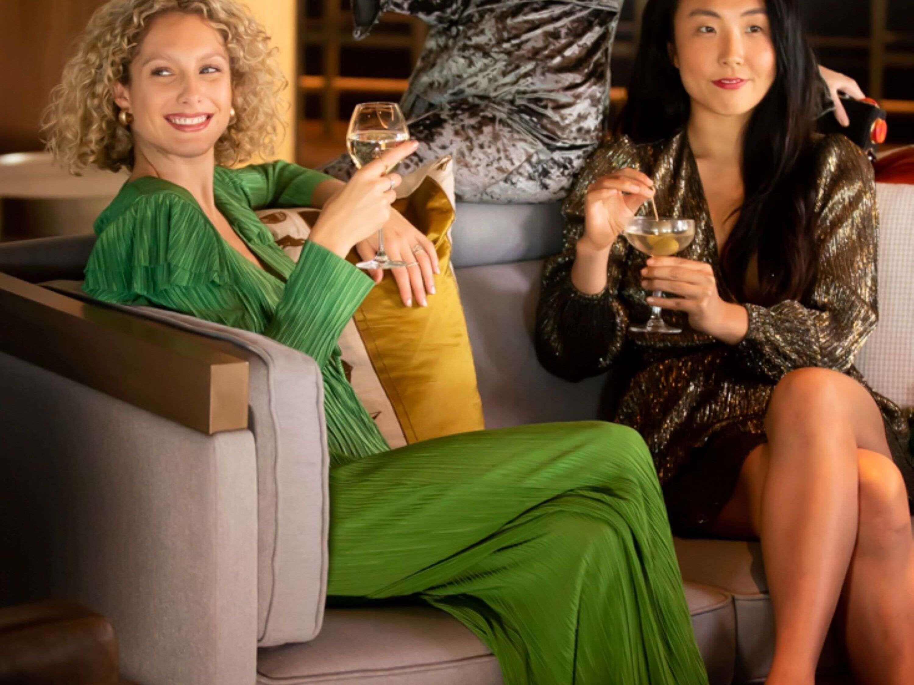 Two people sitting on a sofa with a glass of wine each.