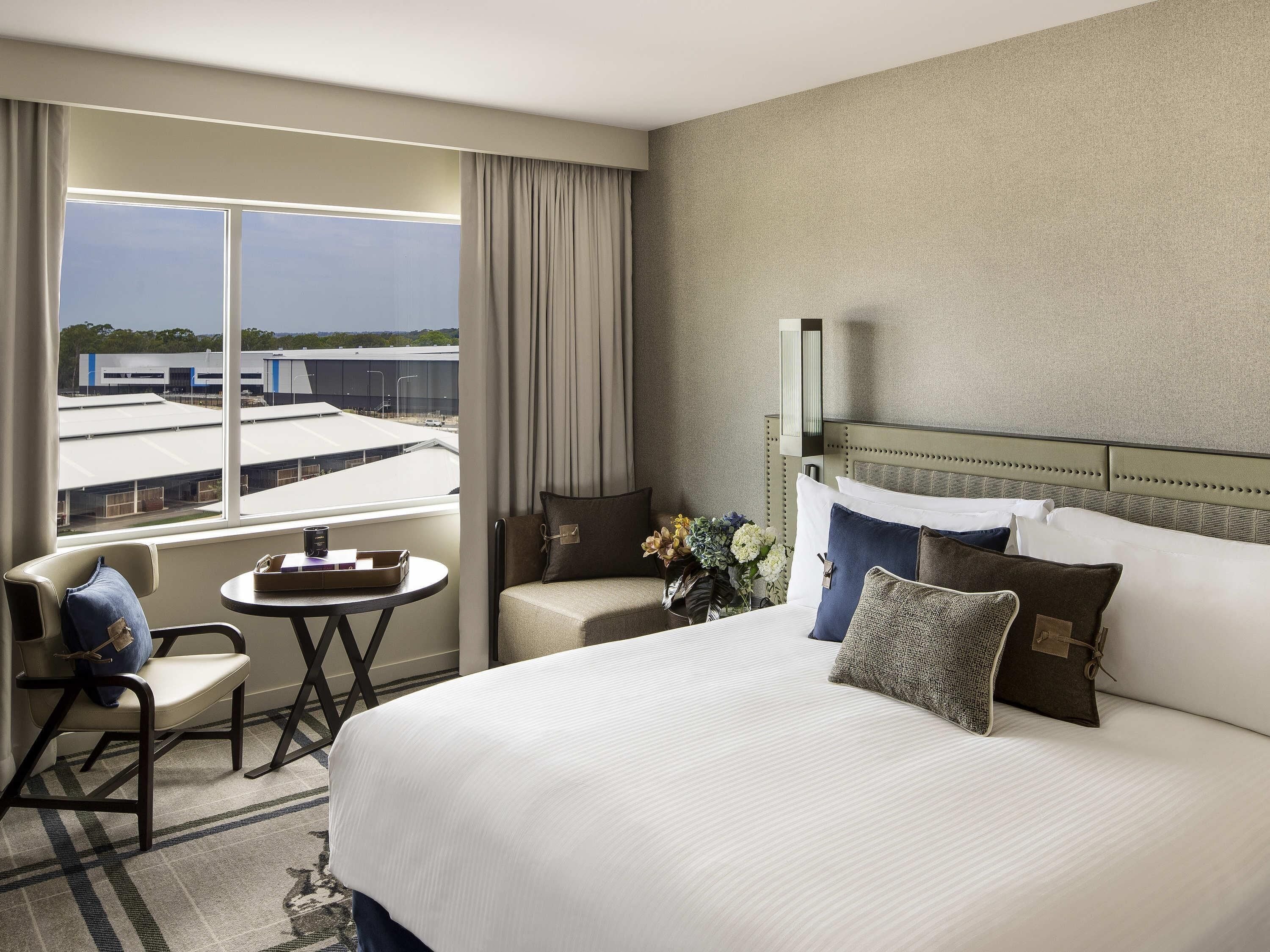 Hotelkamer met een groot bed, een tafeltje, een stoel en uitzicht op gebouwen door het raam.