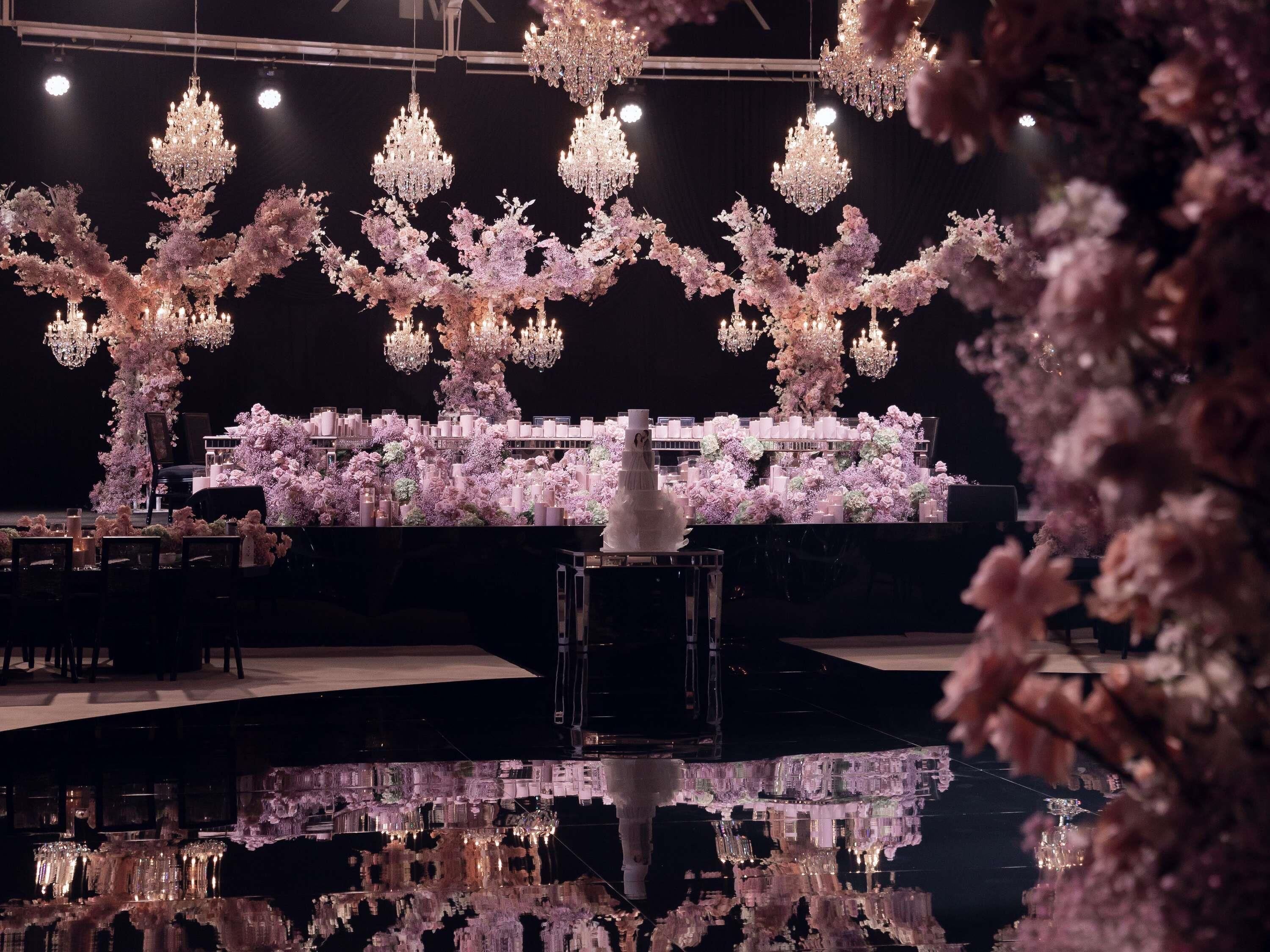 A grand hall with chandeliers, a tiered floral arrangement, and a reflective water feature.
