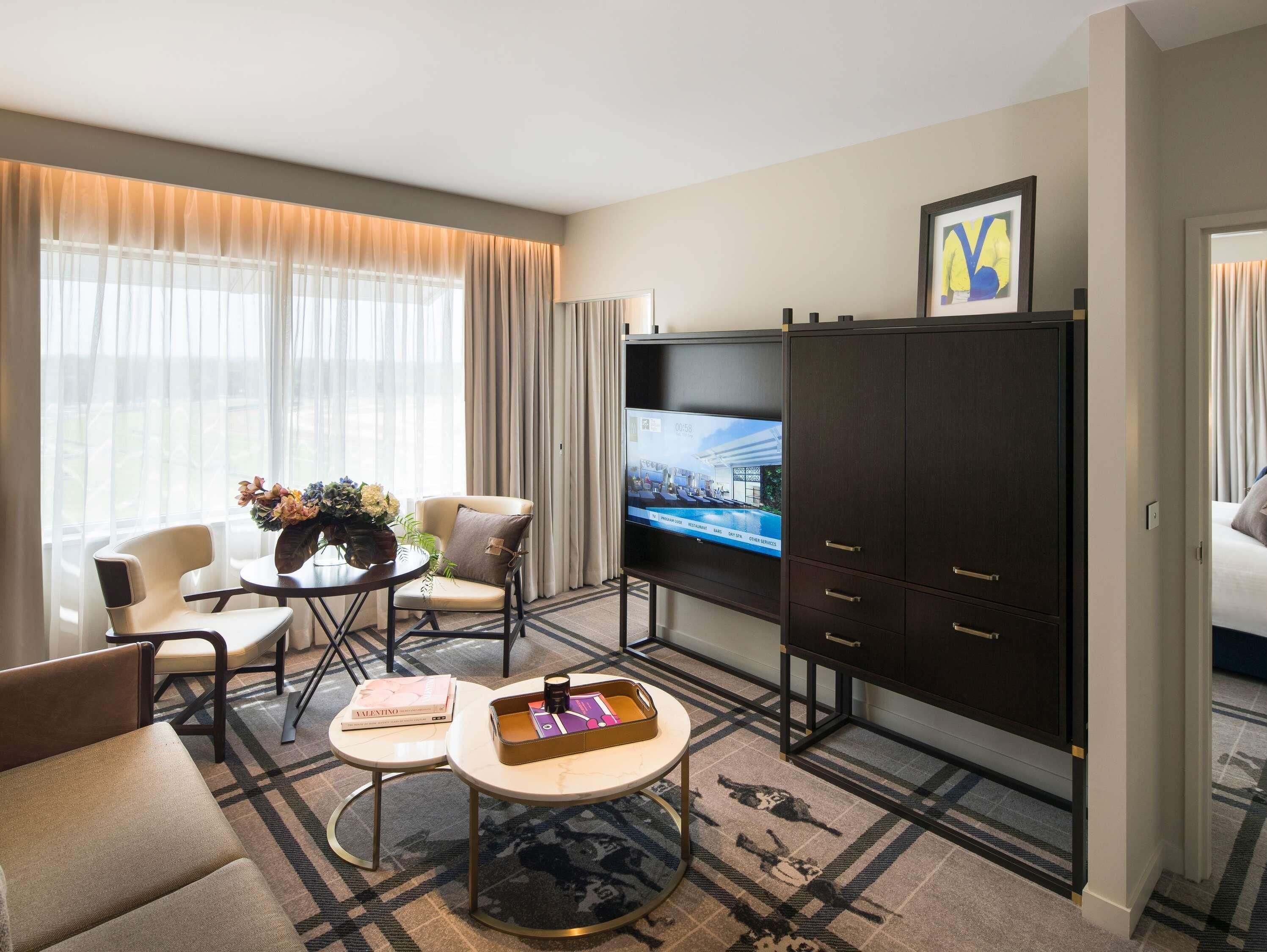 Une chambre d’hôtel comprenant un canapé, deux fauteuils, une table basse, un téléviseur, un meuble et un tableau encadré au mur.
