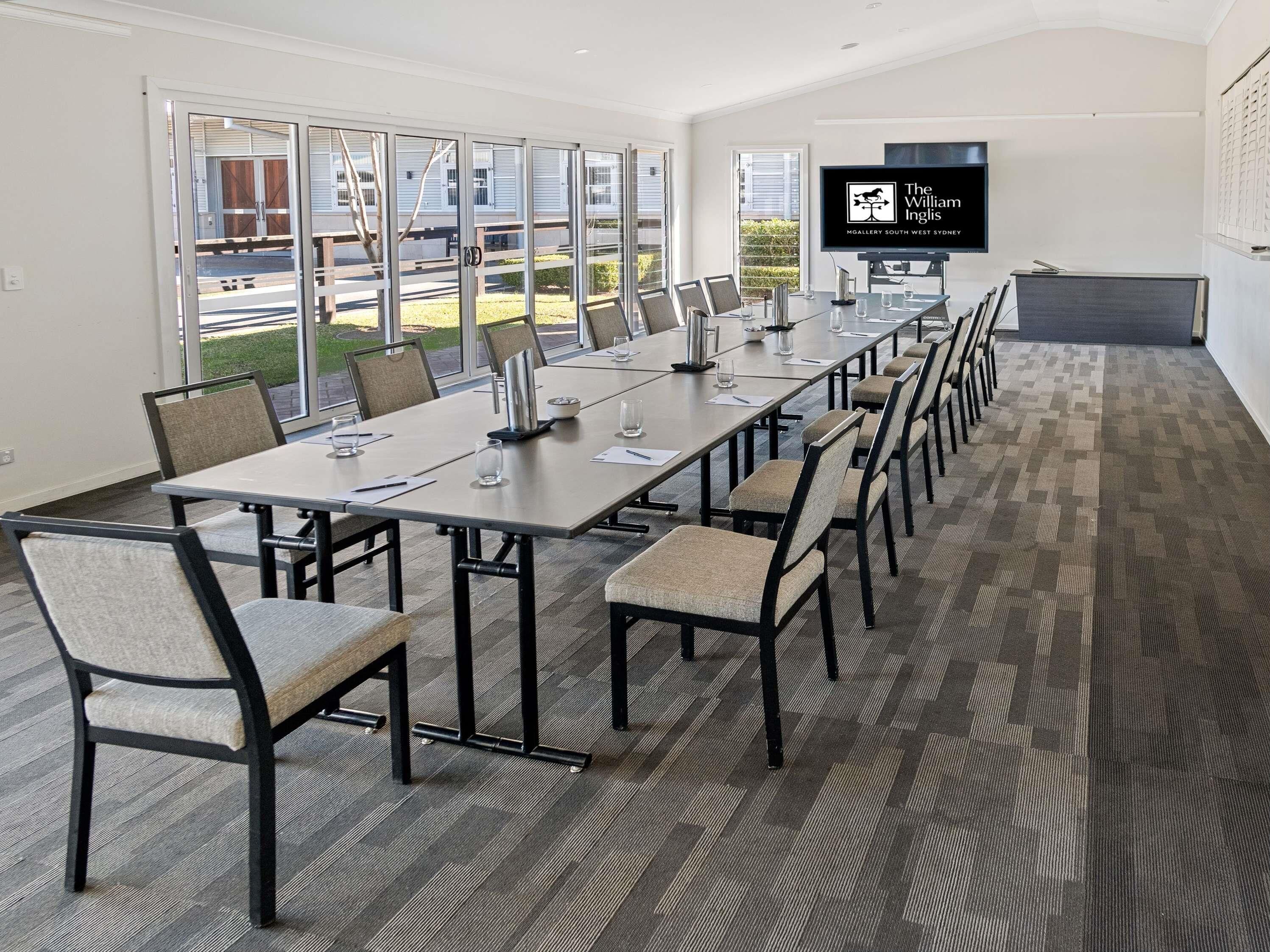 Une salle de conférence avec une longue table, des chaises, un téléviseur à écran plat et une vue sur l’extérieur.