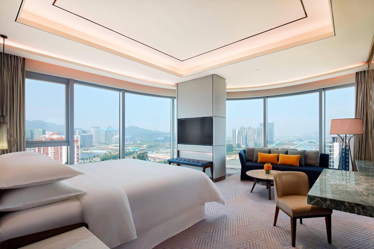 Ein Hotelzimmer mit einem großen Bett, einer Sitzecke, einem Fernseher und Blick auf die Stadt.