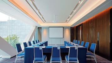 A conference room with a long table, blue chairs, and a projector screen.