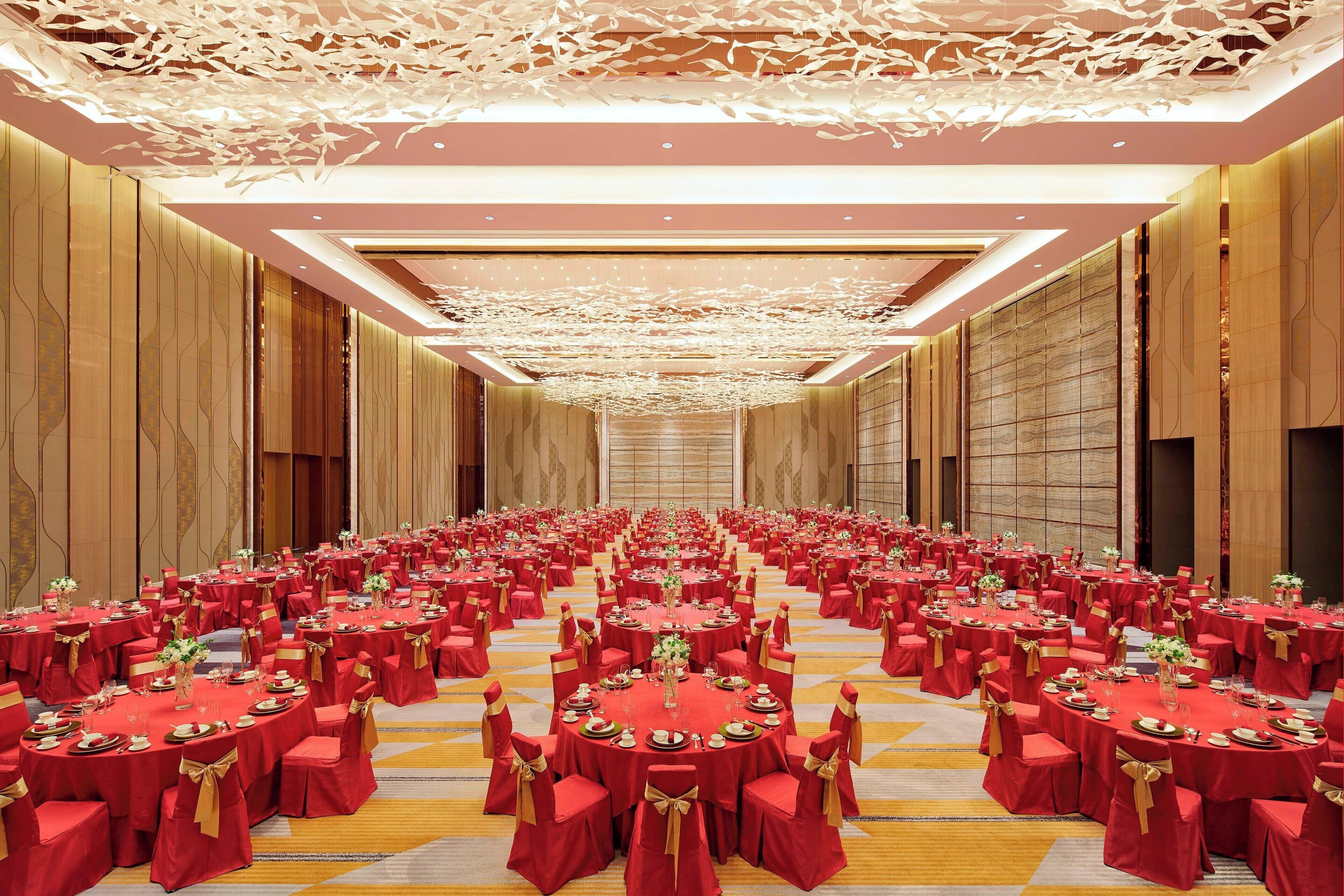A banquet hall with round tables, red tablecloths, and gold sashes.